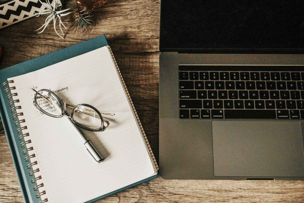 Notebook, eyeglasses, and laptop computer on a desktop.