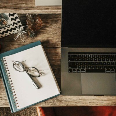 Notebook, eyeglasses, and laptop computer on a desktop.